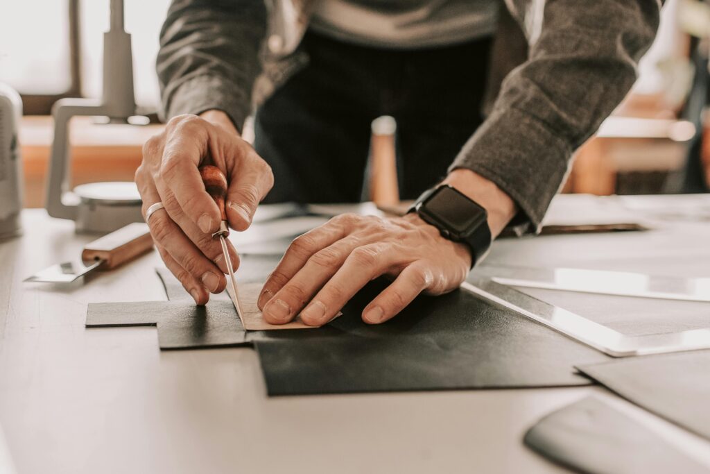 Artisan using an awl for handcrafted leatherwork in a workshop setting.